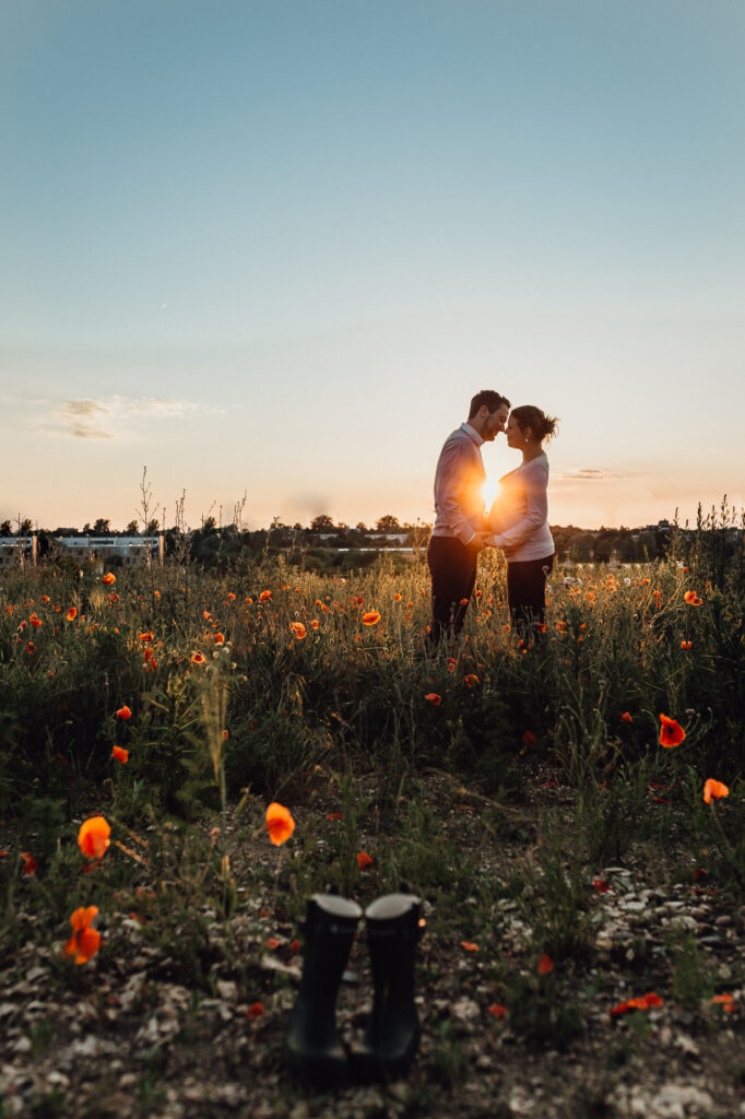 Silhouette eines schwangeren Paares. Im Vordergrund steht ein kleines Paar Gummistiefel. Babybauchfotos in Laatzen.