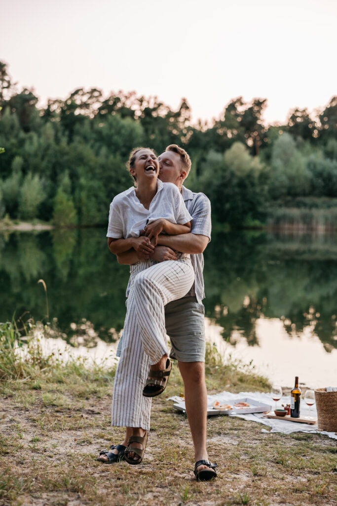 Paar lacht gemeinsam während eines Picknicks am See