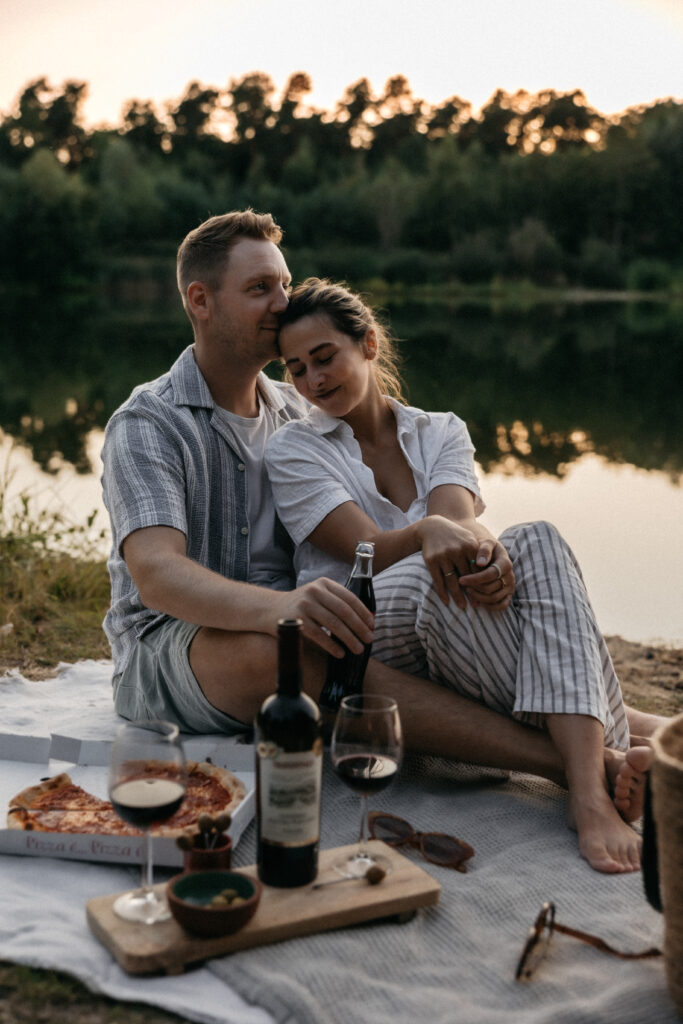 Paar sitzt eng umschlungen auf einer Decke am See im Abendlicht